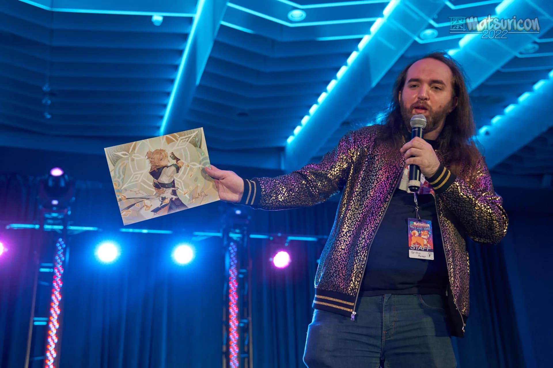 A Matsuricon charity auction host presenting signed artwork from the stage