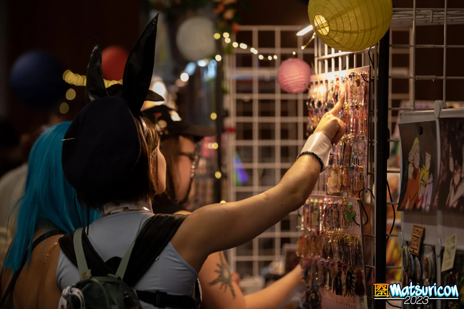 An attendee browsing colorful art displays beneath hanging lanterns inside the Matsuricon Night Market.
