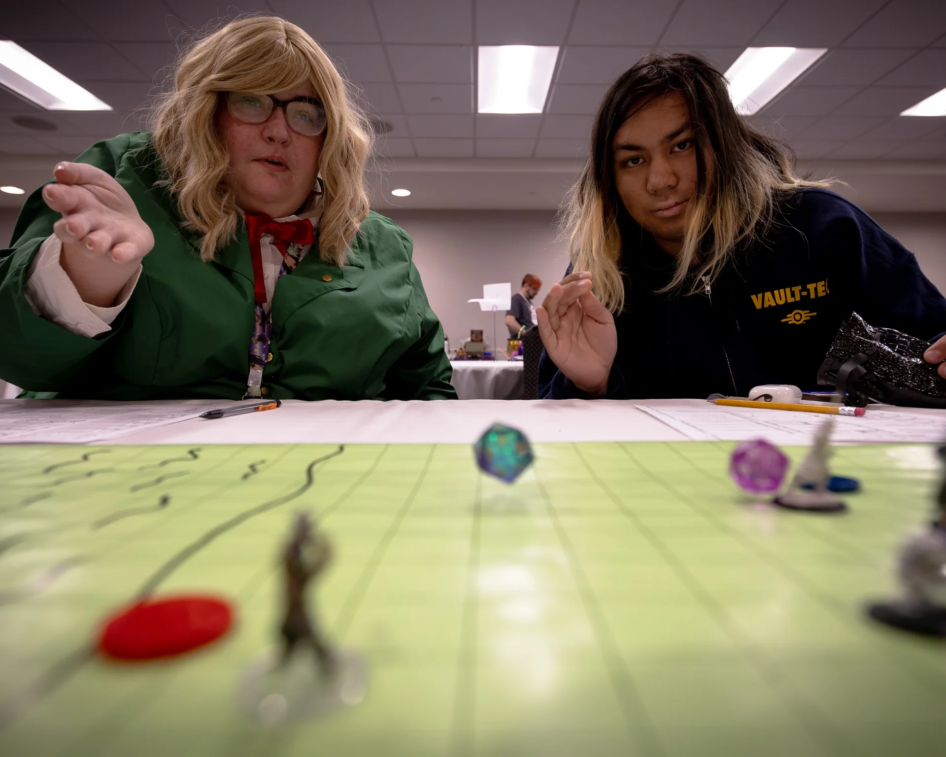 Two Matsuricon attendees react as dice and miniatures move across a tabletop game board.