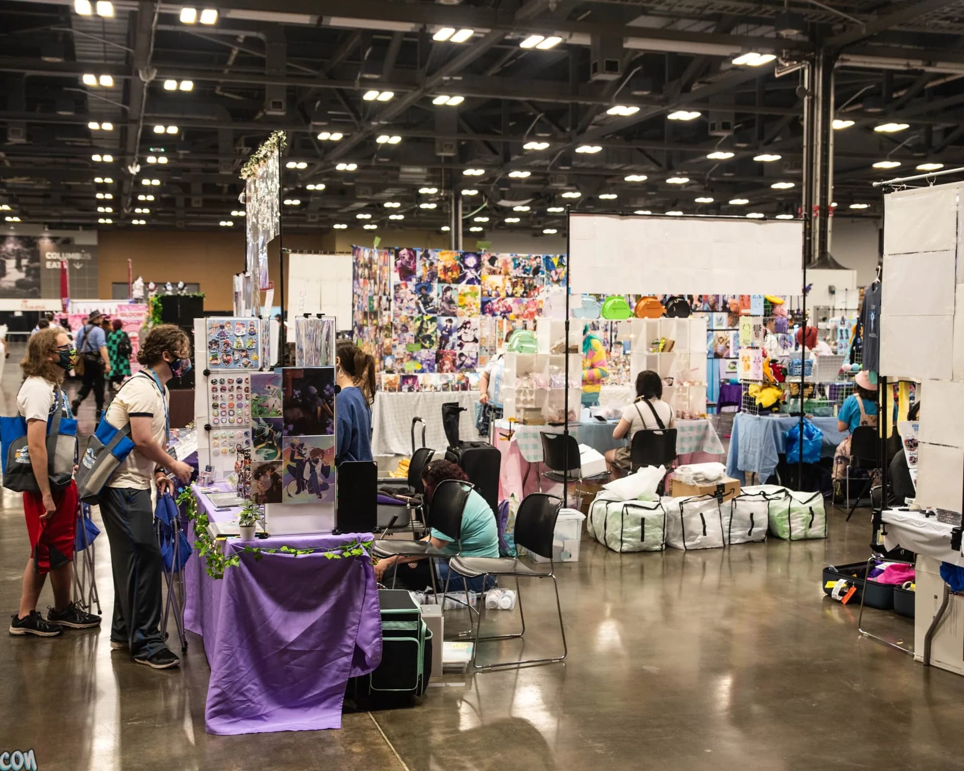 Attendees browse artwork and merchandise displayed at colorful Matsuricon vendor tables.
