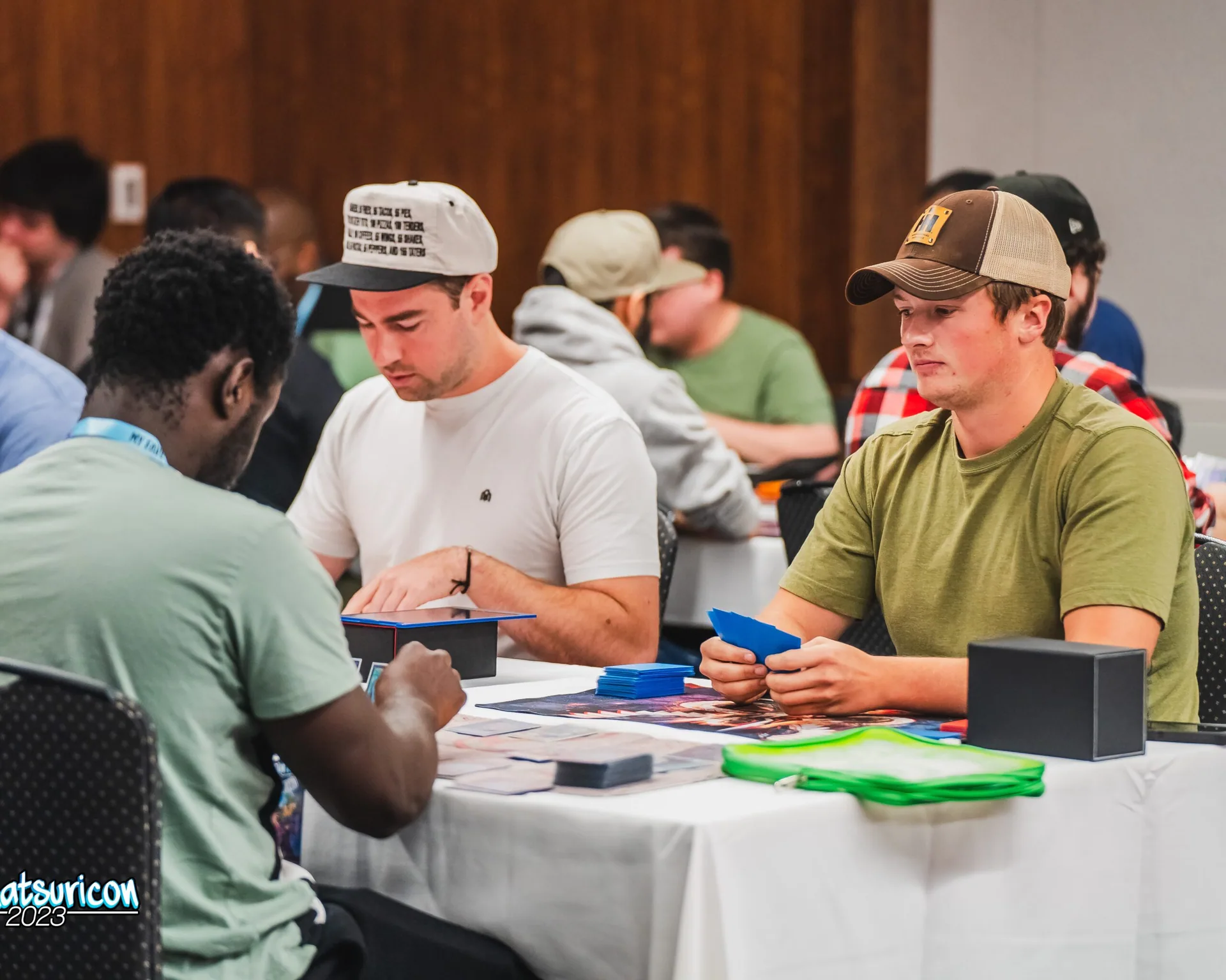Three competitors play a trading card game in the busy Matsuricon gaming room.