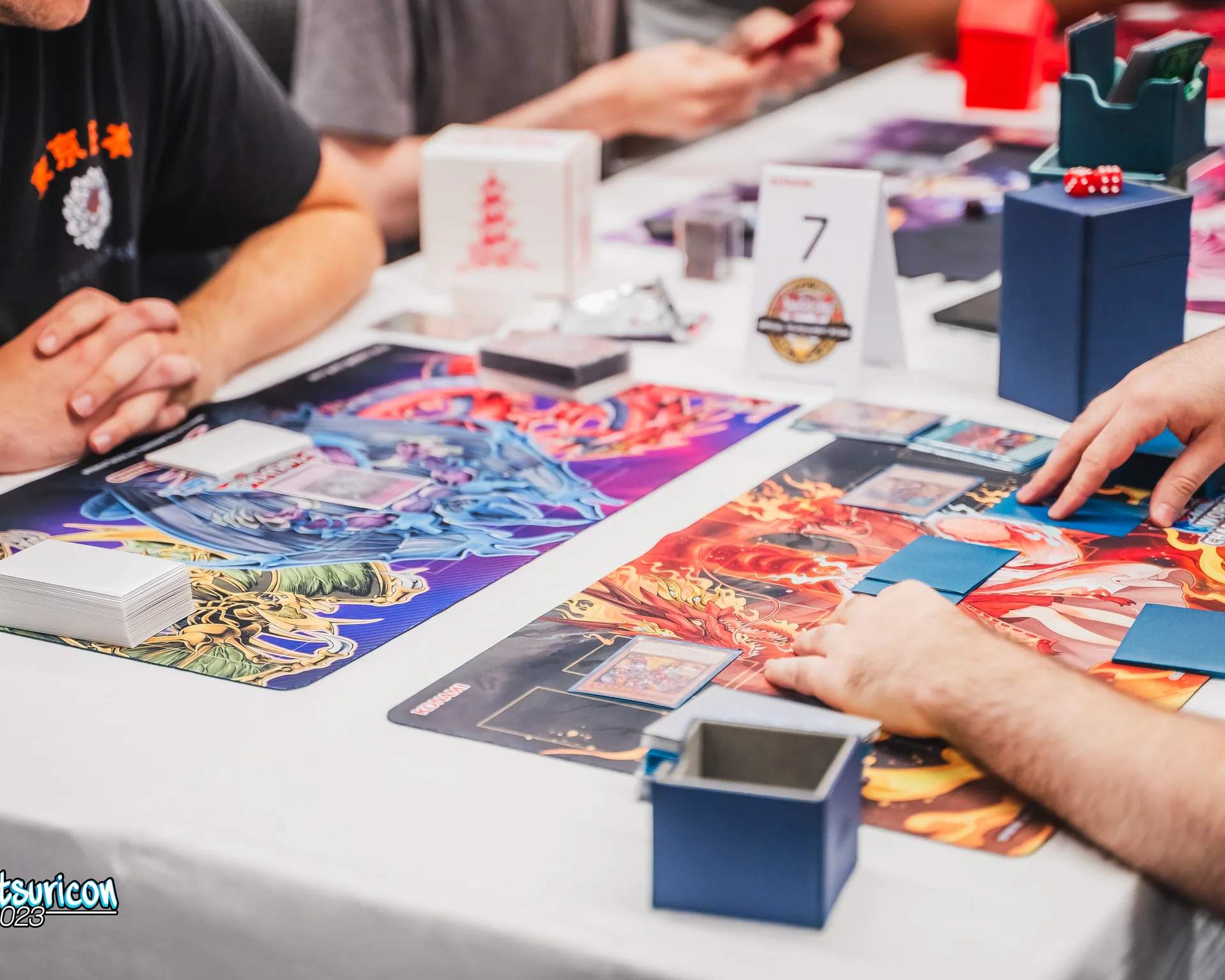Two players face each other across colorful card game playmats during a Matsuricon match.