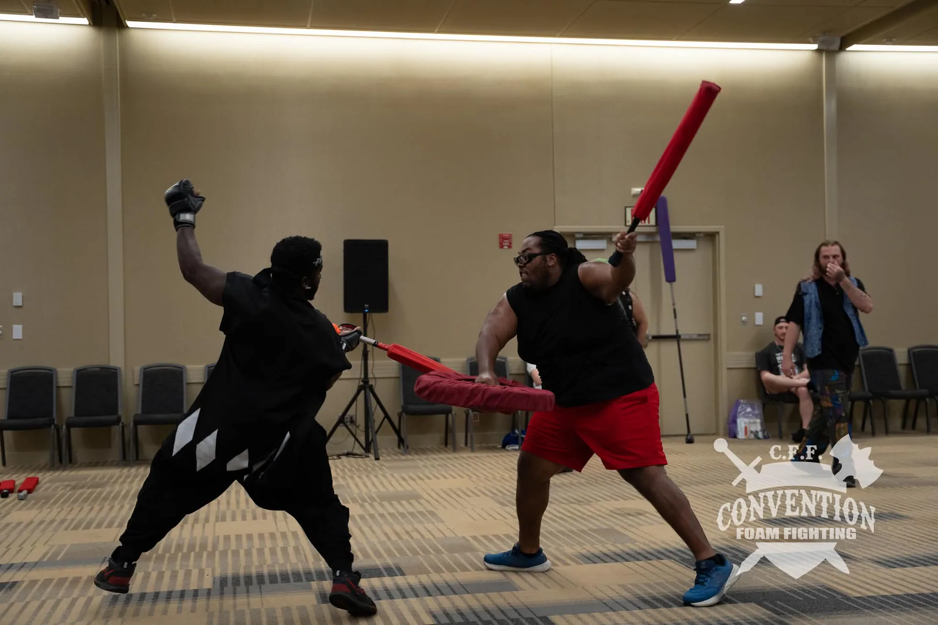 Two Convention Foam Fighting participants duel with red foam weapons and shields in an activity room.